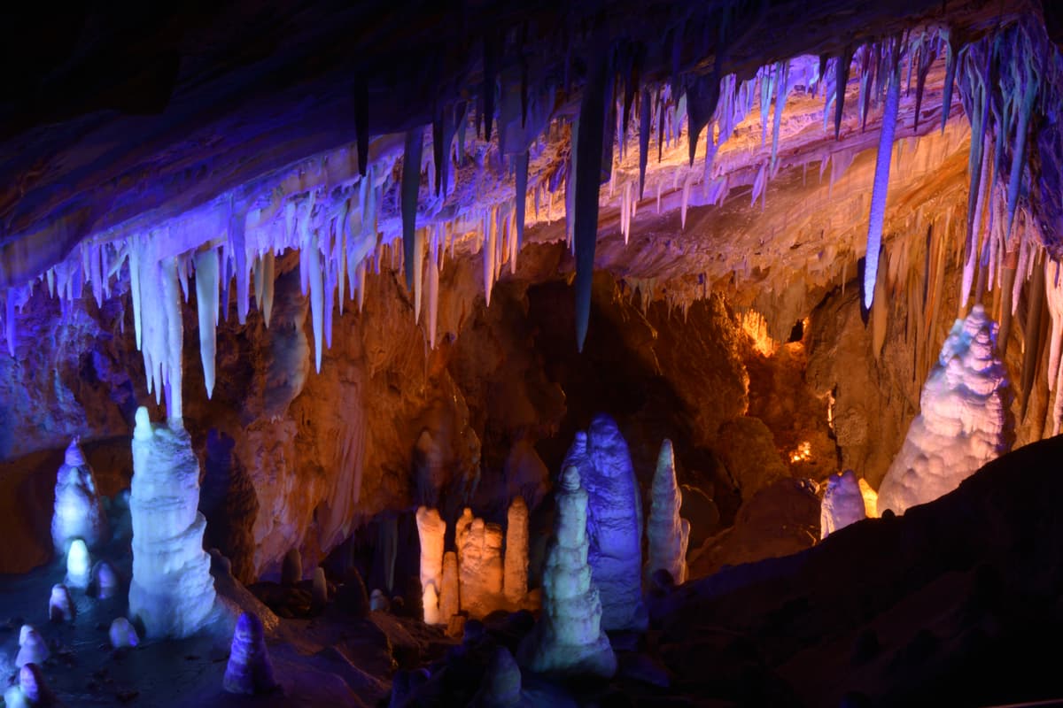 Red-rock stalagmites and stalactites tinted with soft purple and pink lights in the cavers of Glenwood Caverns Adventure Park in Glenwood Springs, Colorado.