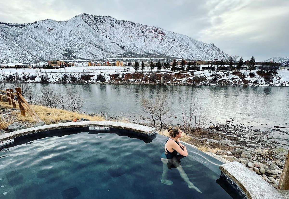 A person leans on the edge of a hot springs pool and admires the winter scenery at Iron Mountain Hot Springs in Glenwood Springs