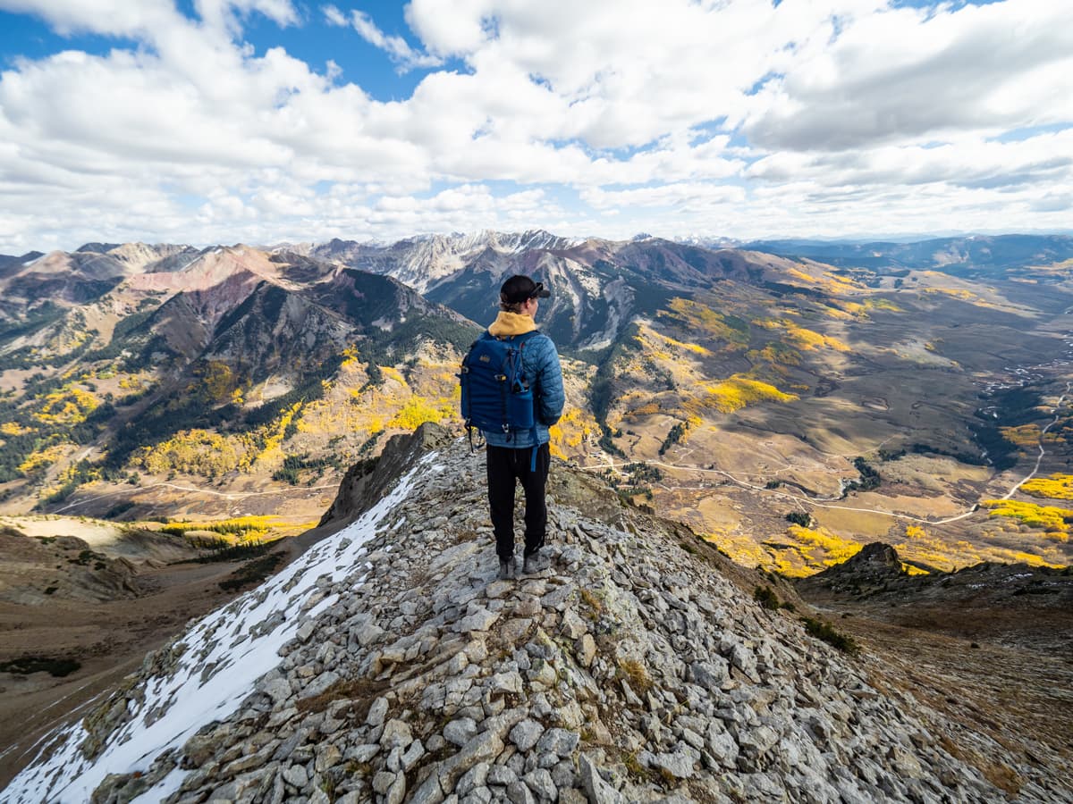 A person stands at the summit of a mountain and admires the patches of golden aspens dotting the Gunnison Valley in Colorado.