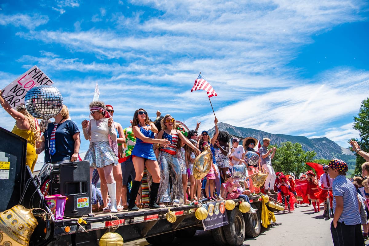 A crowd of people dressed in shiny metallic disco clothes ride on a flat-bed truck in the Crested Butte Fourth of July Parade in Colorado.