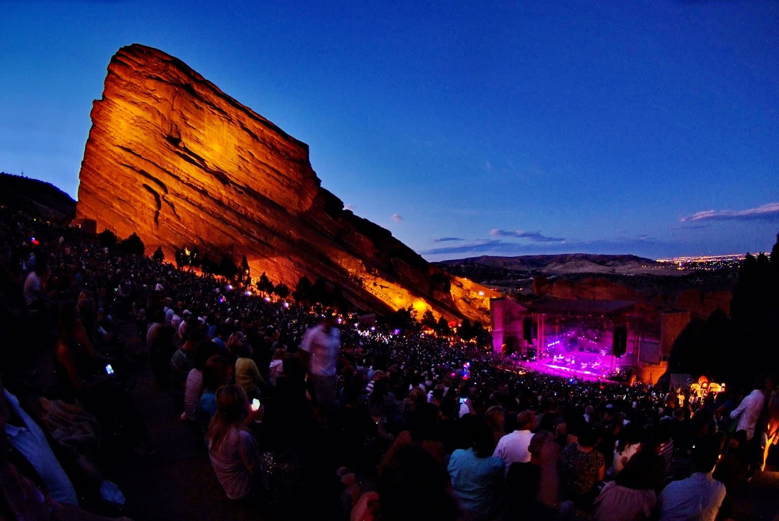 As the sun goes down, lights shine on the jutting red rocks over concert goers