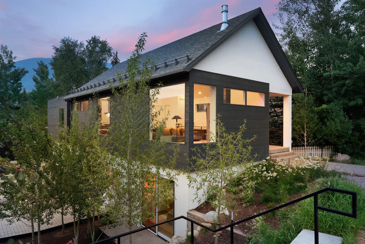 A modern home with glowing lights from the inside, tucked near trees with post-sunset sky colors in Aspen, Colorado.