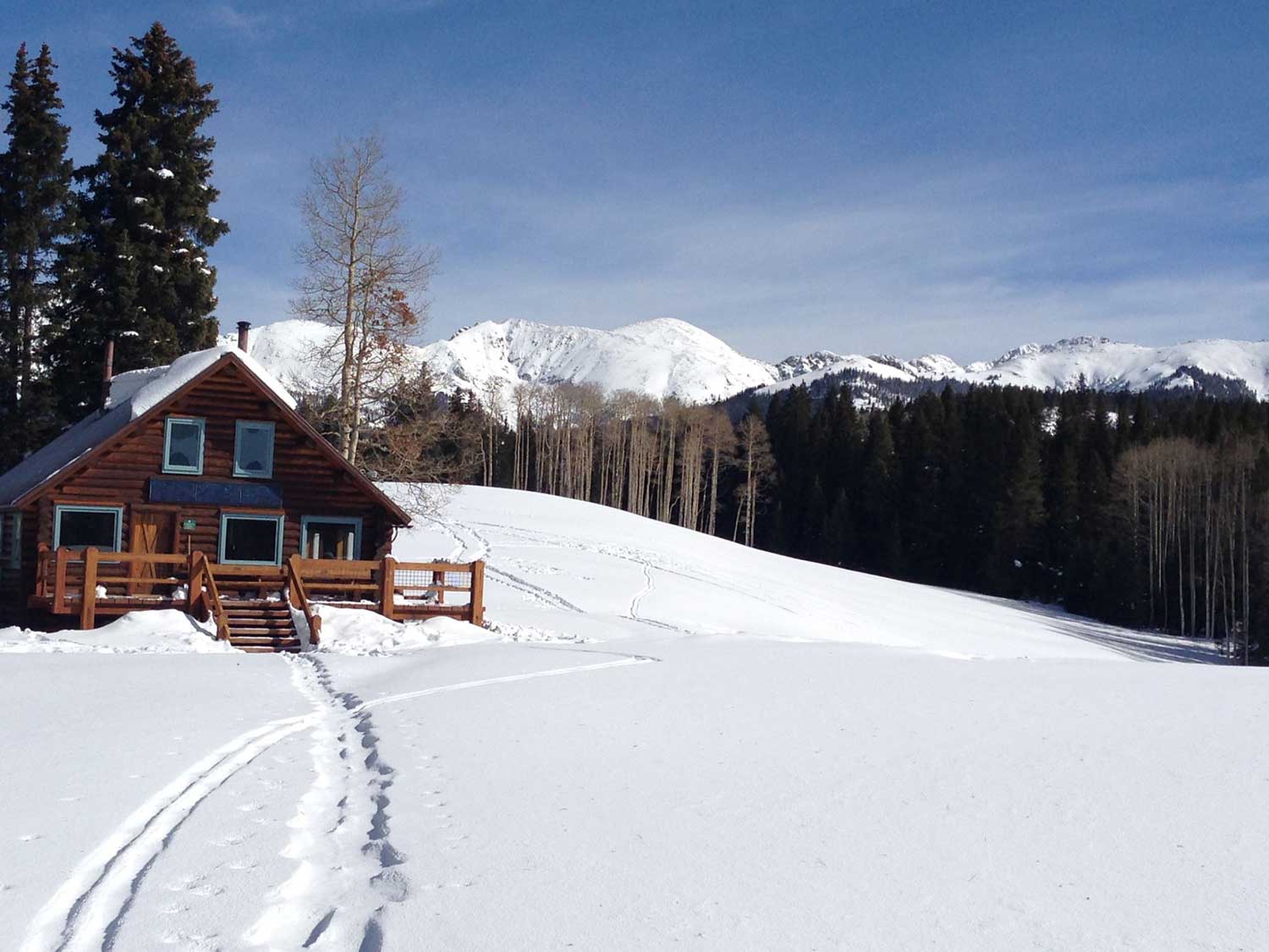 Harry Gates Hut, a wooden hut sitting in among a snowy landscape with soaring snowcapped mountains in the background