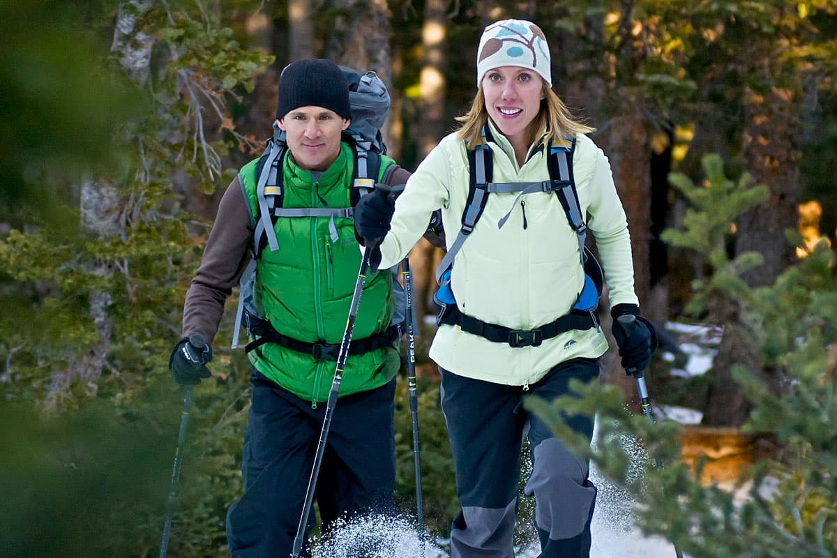 Two people in winter gear snowshoe through Boulder pines