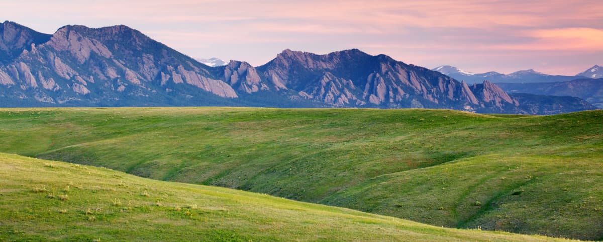 Near Boulder, Colorado, rolling green hills meet the Flatiron rock formations which take on a pink-ish hue in the early morning light.