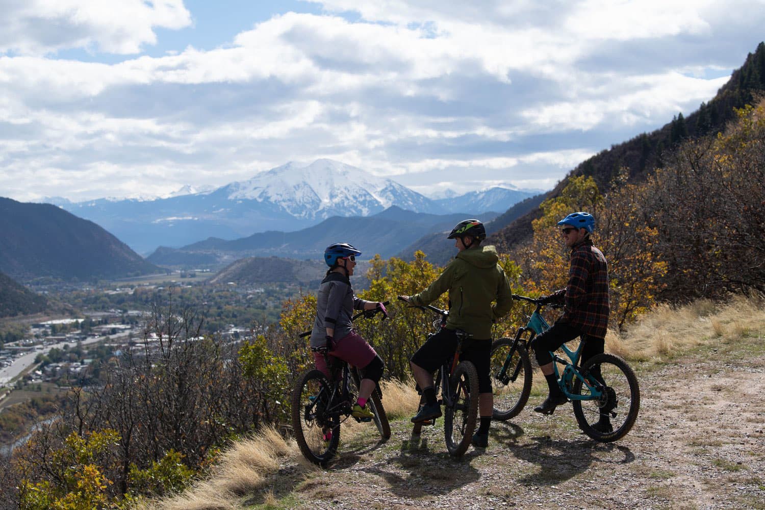 Three bikers pause and dismount to look at a snowcapped mountain view in Glenwood Springs