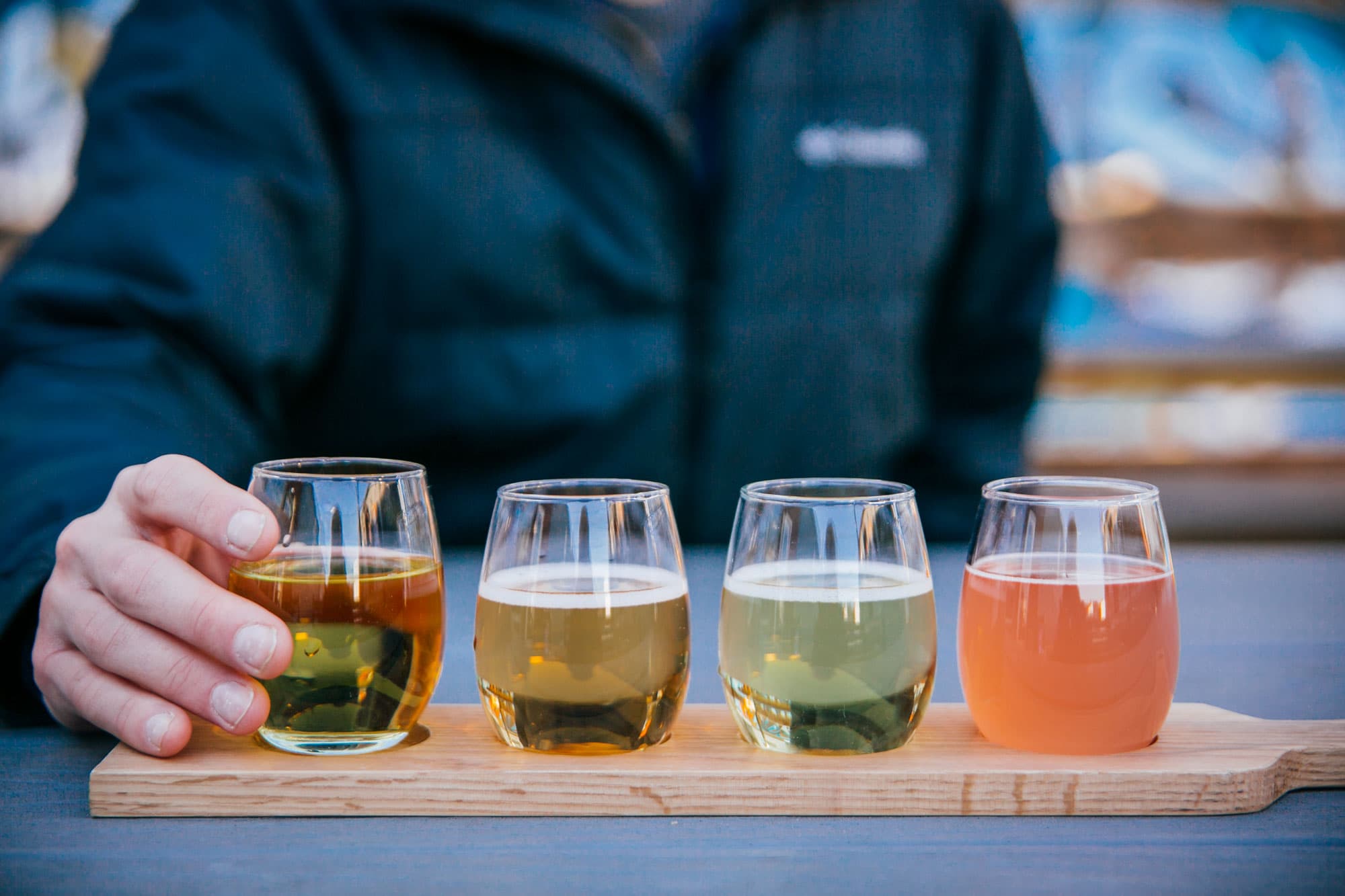 Four stemless wine glasses are each filled with a different type of cider and sit on a wooden tray at Stem Ciders in Denver, Colorado.