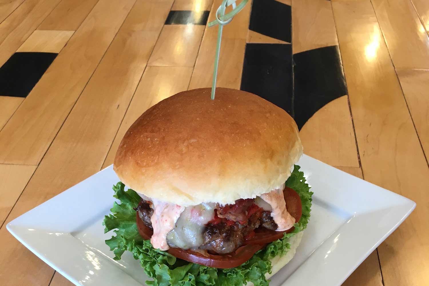A burger with melty cheese and sauce sits on a wood table at Bingo Burger in Pueblo