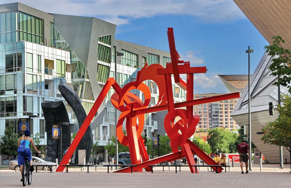 A piece of public art by Mark di Suvero sits in a plaza in Denver, Colorado, and features a metal tangle of red geometric shapes.