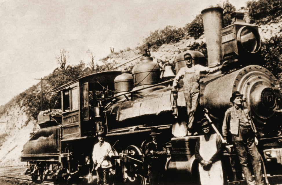 A black-and-white historic photo of a man sitting on a locomotive