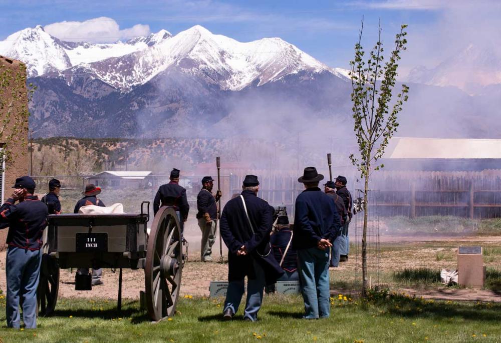 People dressed in antique war uniforms watch as smoke clears from a fired cannon at Fort Garland Museum & Cultural Center.