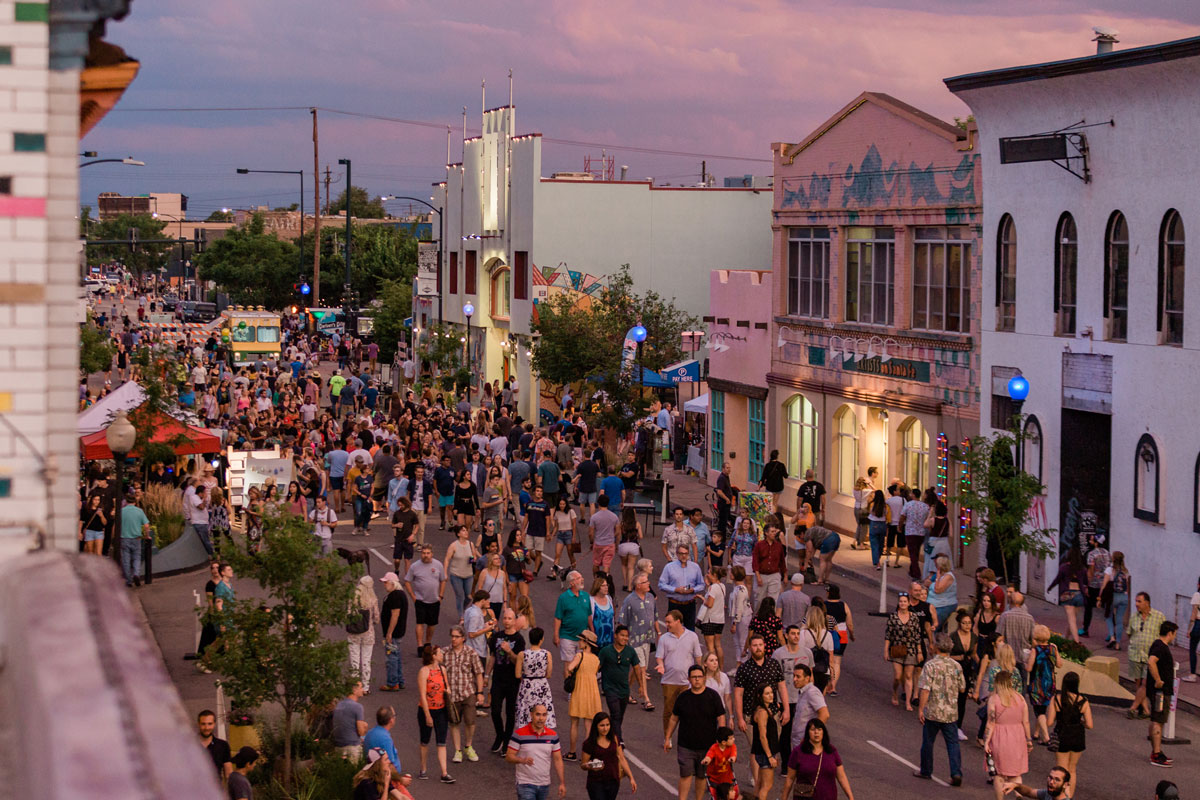 As the colors of the sunset fade from the clouds overhead, crowds of patrons meander and mingle in the street during the First Fridays art walk in the The Art District on Santa Fe in Denver, Colorado.