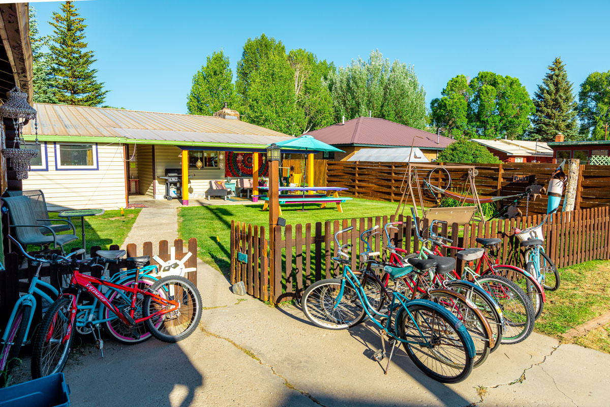 Deep red and vibrant, light-blue bikes are neatly parked against a low, brown picket fence at the Wanderlust Hostel in Gunnison, Colorado.
