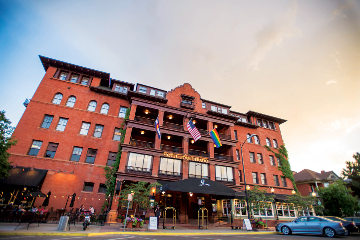 The red-bricked and multi-story Hotel Boulderado stands tall in Boulder, Colorado. Green ivy creeps up two sides of the hotel. Three flags fly from a balcony.