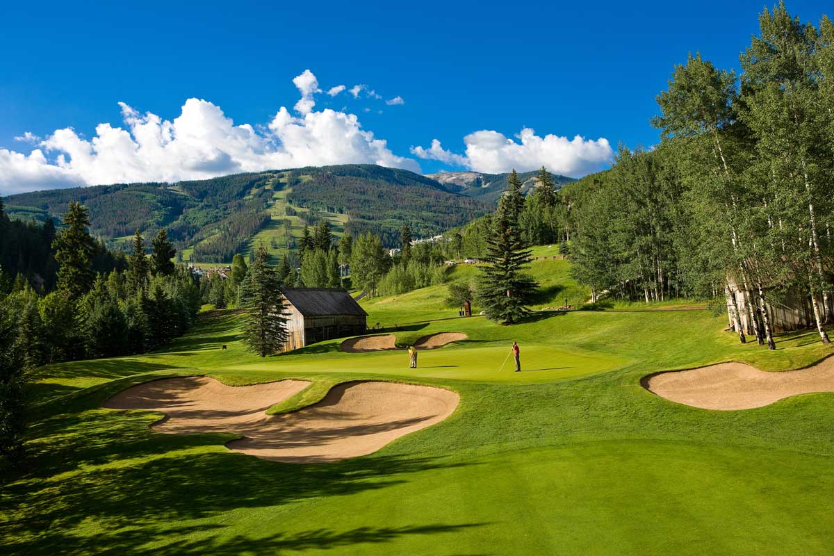 Two golfers practice their skills on a putting green at Beaver Creek Golf Club. They're surrounded by a thick forest of tall trees.
