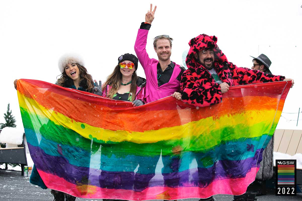 Aspen Gay Ski Week attendees stand behind a rainbow Pride flag