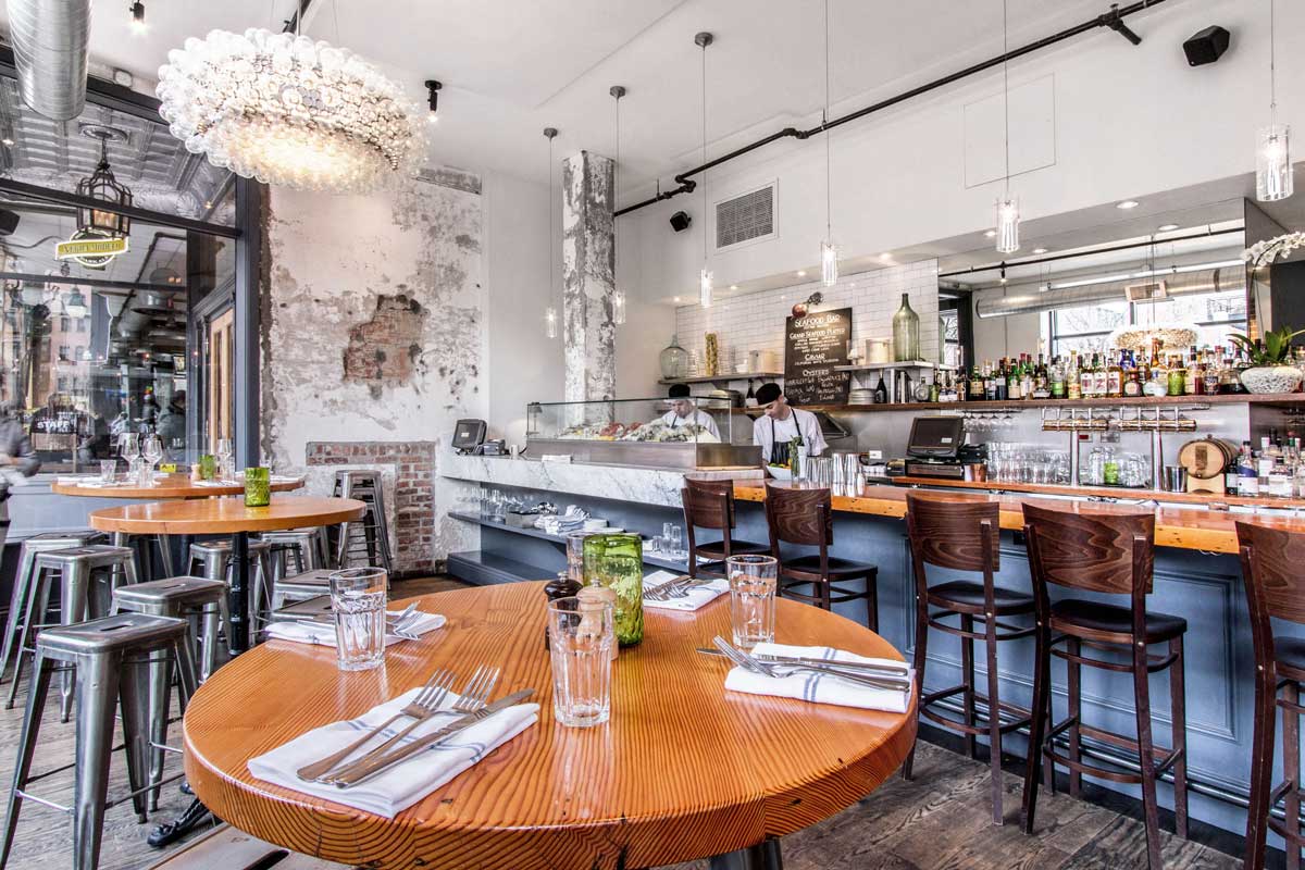 White subway tile, warm-wood tables and empty bar stools await patrons