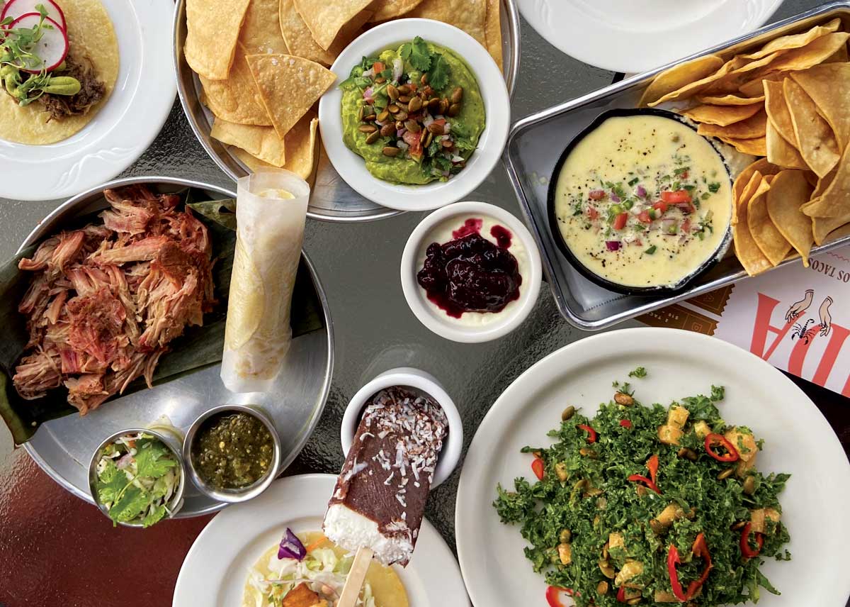 A table piled high with Latin menu items, including bowls of guacamole and tortilla chips, white queso, succulent meats and more, at Cantina Loca in Denver, Colorado.
