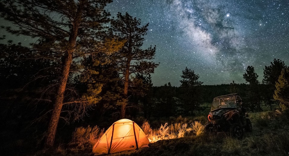 A camping tent and ATV under the night sky of bright stars