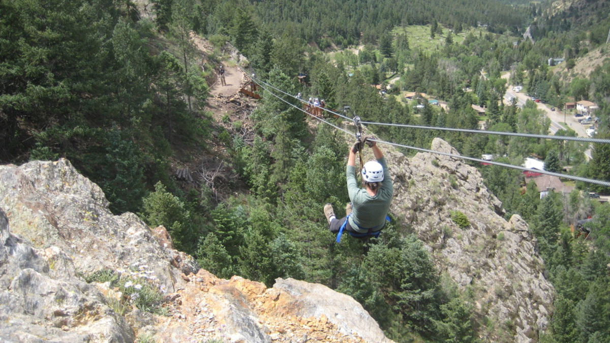 A zipliner zooms down the deep Mountaintop Zipline course over a deep-looking valley within the deep-green pines at the Buena Vista outpost with AVA Rafting & Zipline.