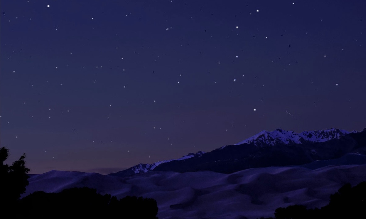 The Big Dipper star constellation on a deep purple night sky above snowcapped mountains and sand dunes