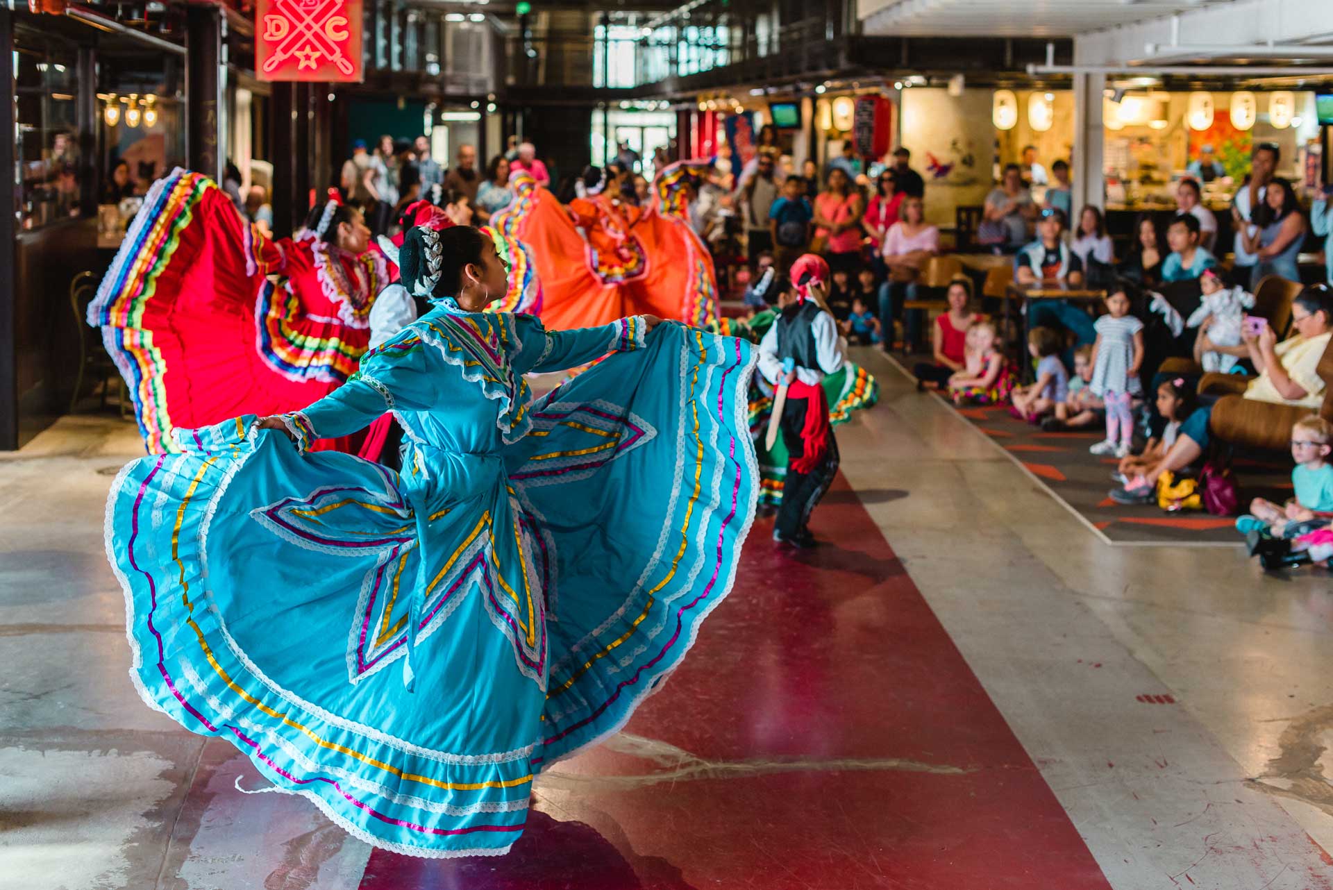 Dancers in bright red and blue dresses twirl their skirts in front of a gathered audience