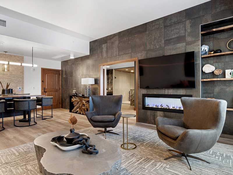 A hotel suite with two cozy chairs in front of a fire and large TV