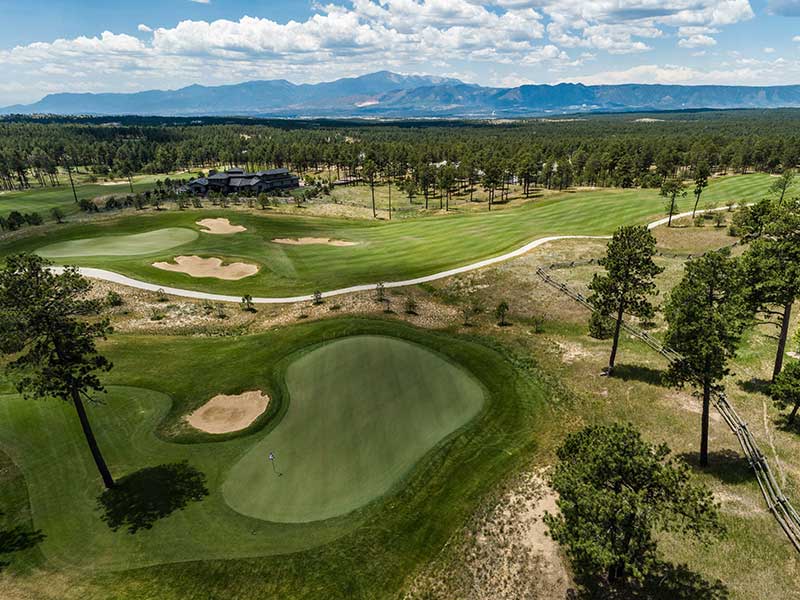 Under a blue sky with puffy white clouds, an empty golf course is a splash of green