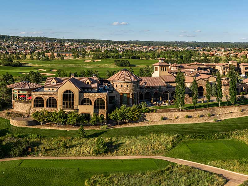 A castle-like resort of brick buildings sit amid a golf course under blue skies