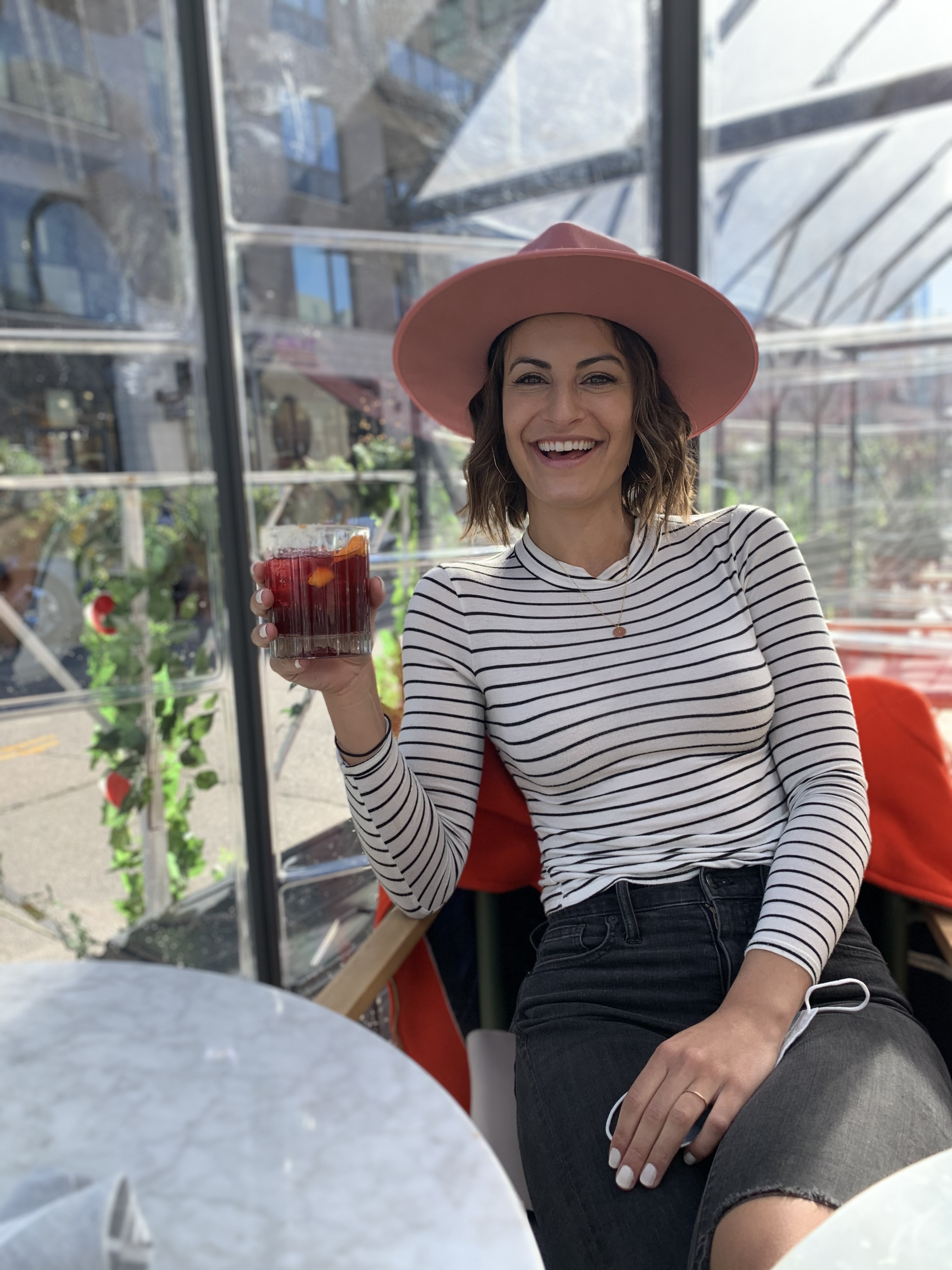 A person in a long sleeve striped shirt and hat laughs on a chair under the sun with a drink in hand at the Halcyon.