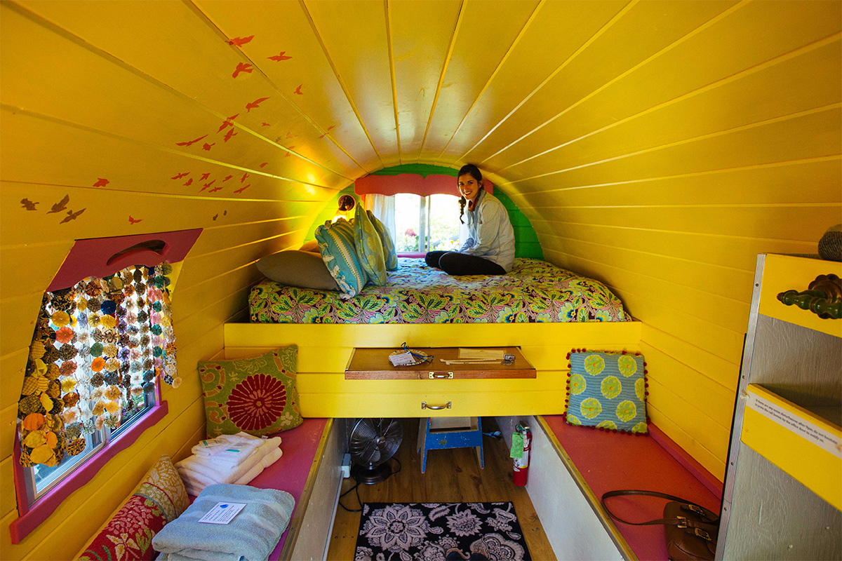 A weary traveler sits on a bed beneath a sunflower-yellow, wood-paneled curved ceiling at Avalanche Ranch near Redstone, Colorado.