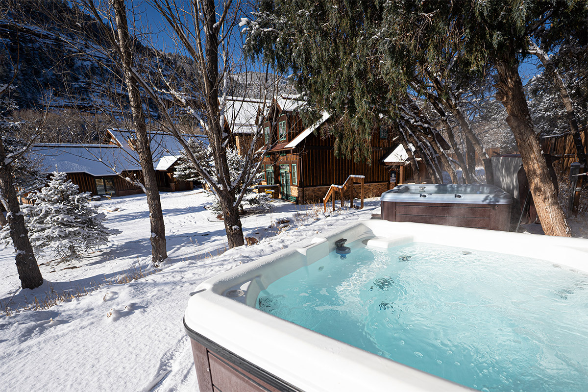 Clear, blue-tinged water bubbles gently in one of two hot tubs underneath a stand of pine trees outside The Bivvi Telluride in Colorado.