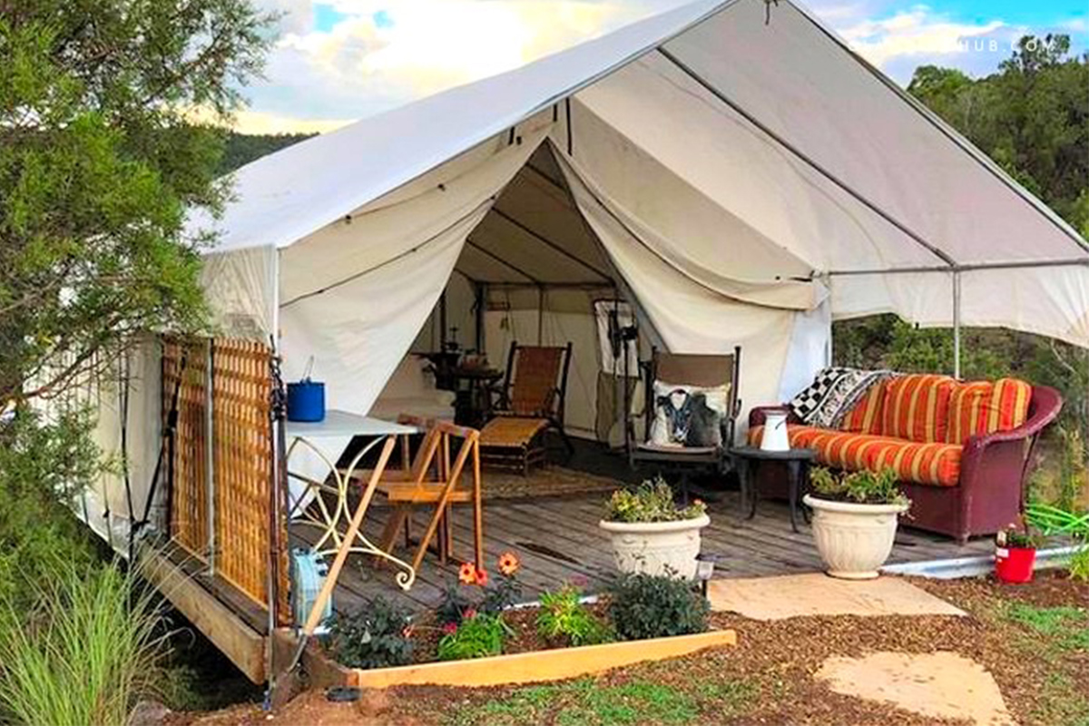 A safari-style tent with a small front porch is set up for guests at Cedar Ridge Ranch in Colorado. The tent features plush, cushioned seating and some decorative plants.