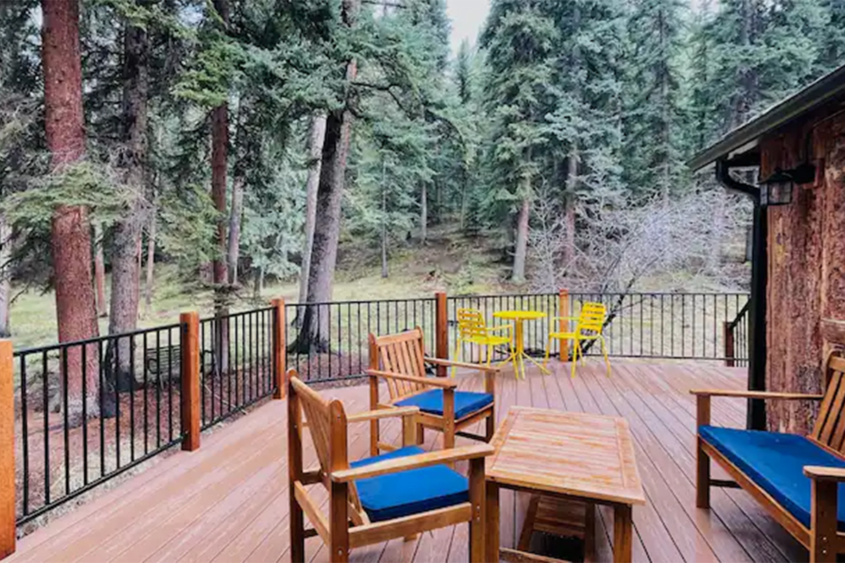 Two yellow chairs and a set of wooden patio furniture with blue cushions are positioned on a cabin porch near Conifer, Colorado.