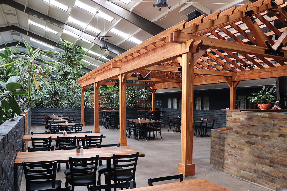 An outdoor-style dining patio is set up near a wooden pergola in the tropical-plant-filled atrium at the Historic Cow Palace Inn in Lamar, Colorado.