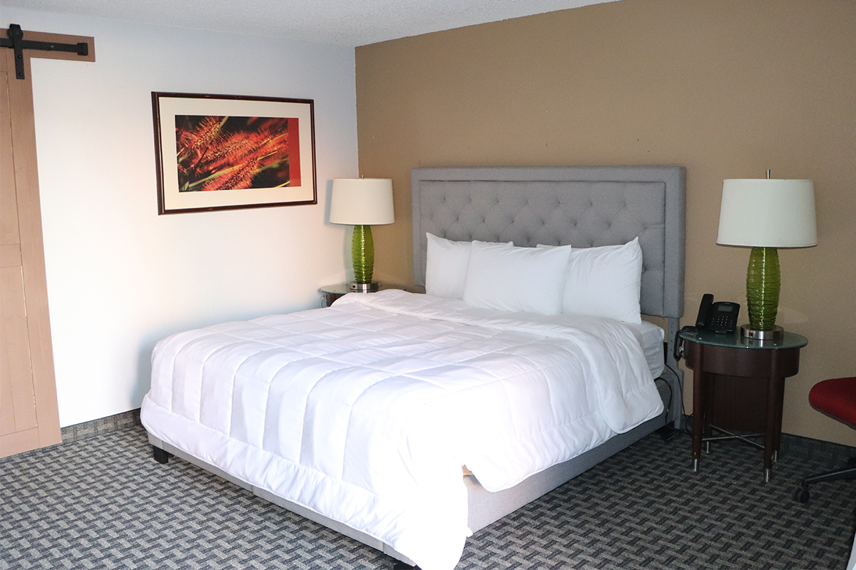 A bed with cozy, white linens and a gray, fabric headboard is made up and ready for guests at the Historic Cow Palace Inn in Colorado.