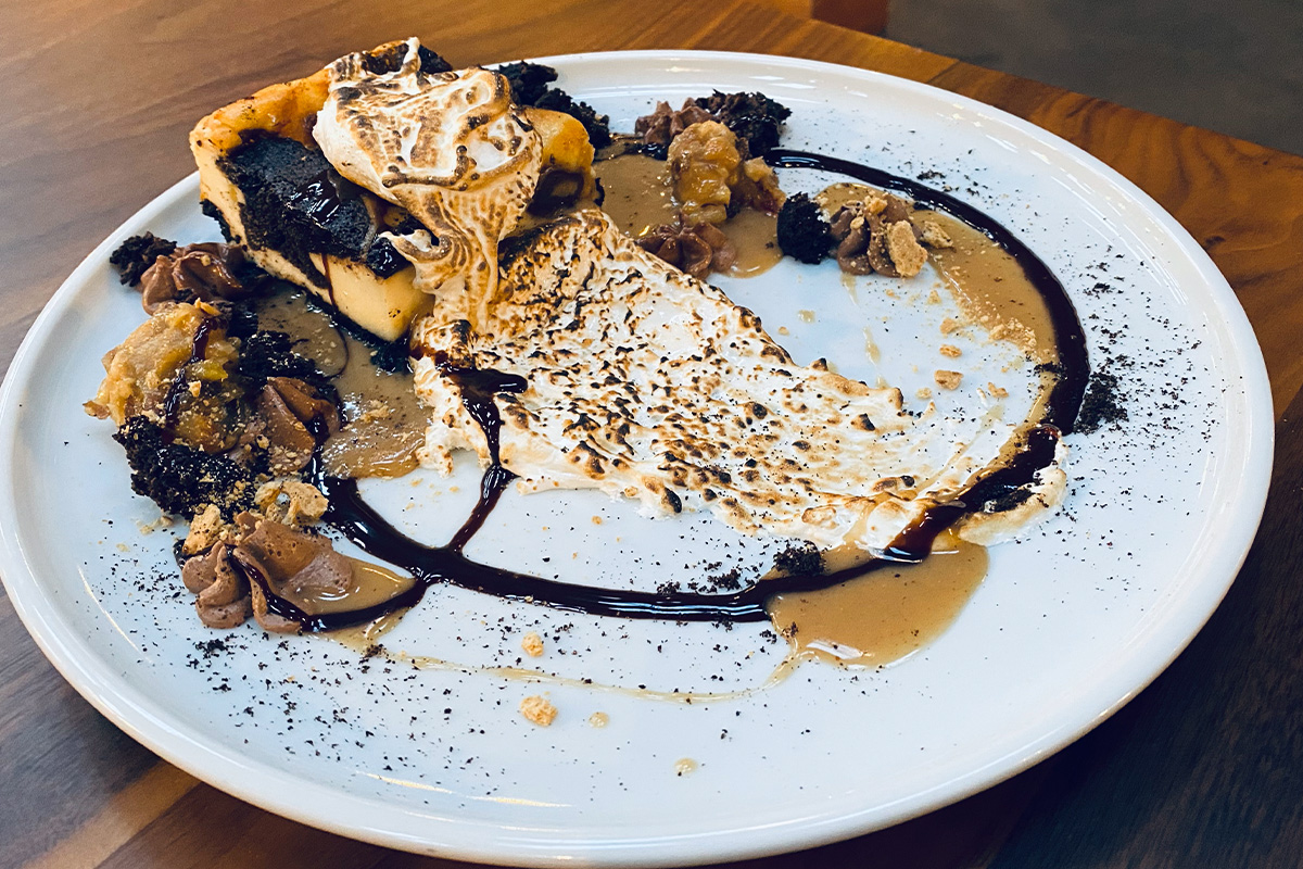 A decadent brownie with a gooey, flame-charred marshmallow on top and decorative chocolate sauce sits on a plain, white plate at the Historic Cow Palace Inn in Lamar, Colorado.