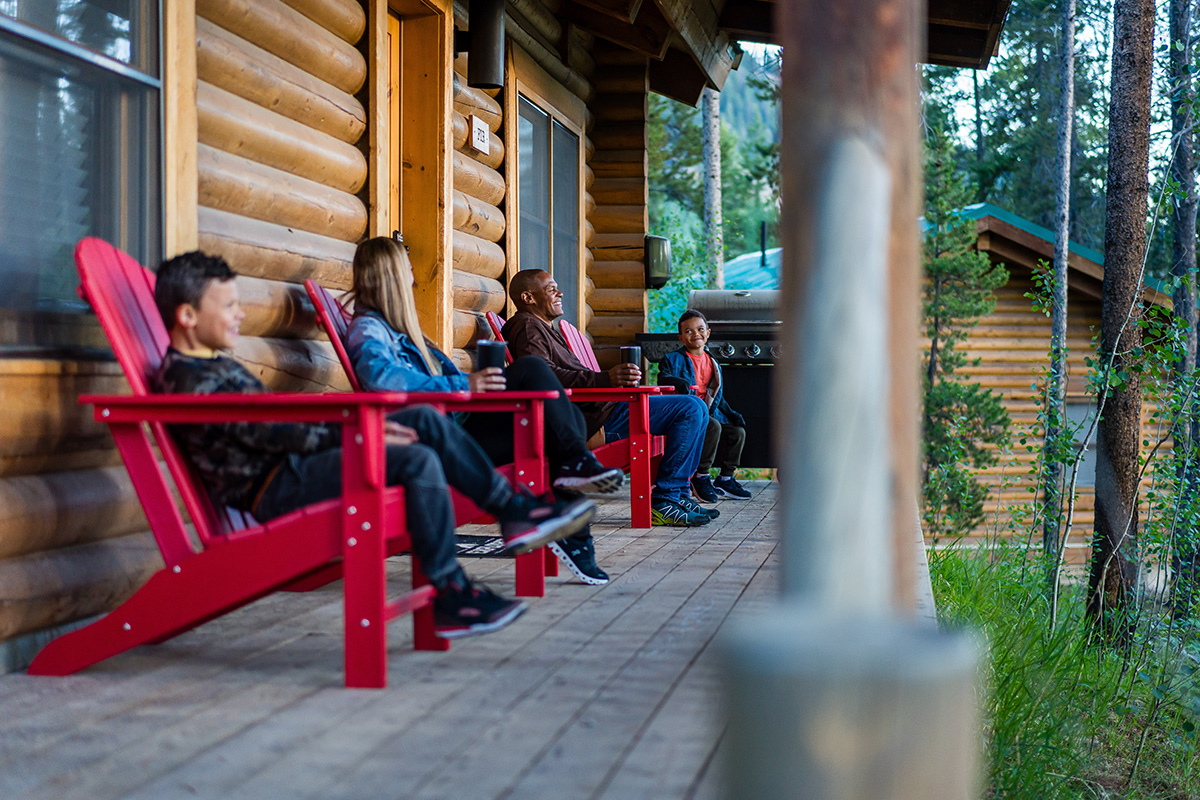 A family of four relaxes in red Adirondack chairs on a cabin porch at Camp Hale near Red Cliff, Colorado.