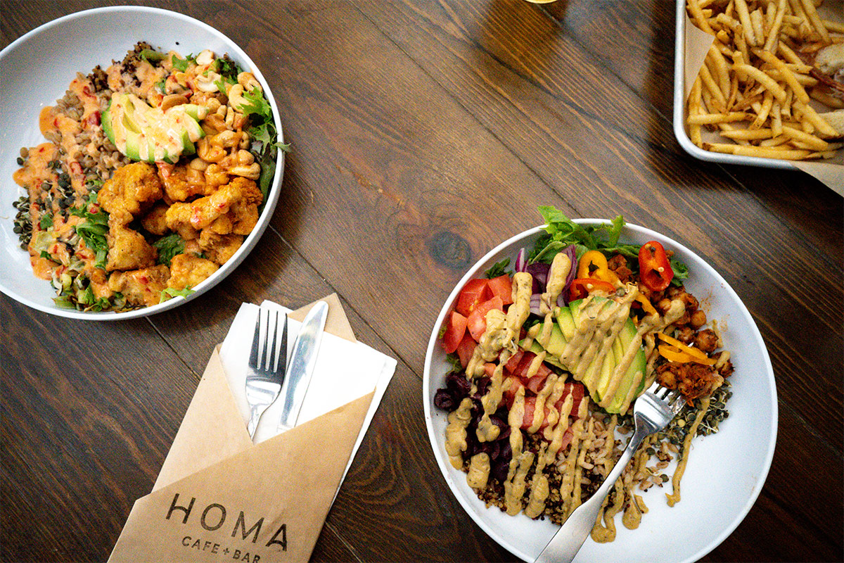 Two plates of delicious food drizzled in sauce sit on a table at the Homa Cafe + Bar on the ground floor of Kinship Landing.