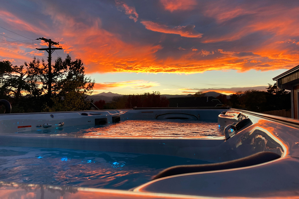 Vibrant oranges and pinks dye the clouds in a view from the waters of a heated pool-hot tub combination in the gardens of The Oasis on Eisenhower.