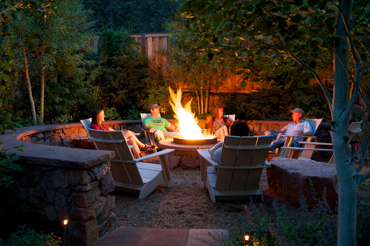 Guests of the Outlook Lodge sit around a campfire. Their faces are illuminated by the bright orange flames of the fire.