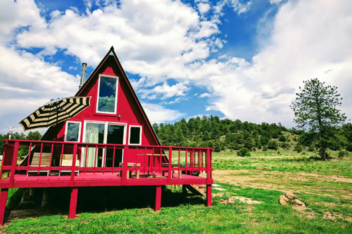 It is summertime and the outdoors are green with grass and leaves. A cherry-red A-frame building near Westcliffe, Colorado awaits guests.