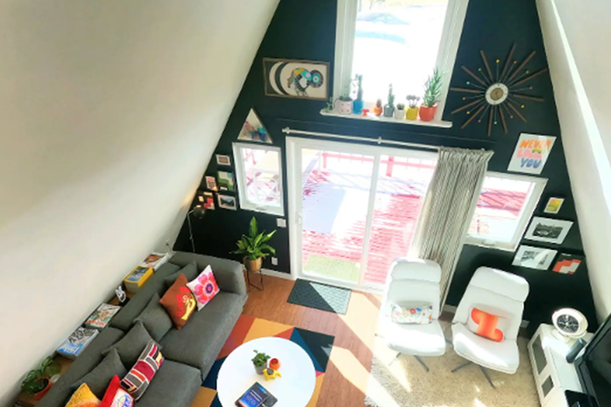 A living room in an A-frame building is decorated with retro vibe. Bright light shines through the tall windows of the building near Westcliffe, Colorado