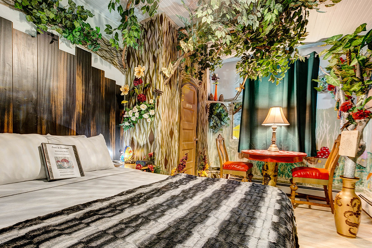 The green-leafed branches of a fake tree spread across the ceiling of the woodland-themed Enchanted Forest room at The Oasis on Eisenhower