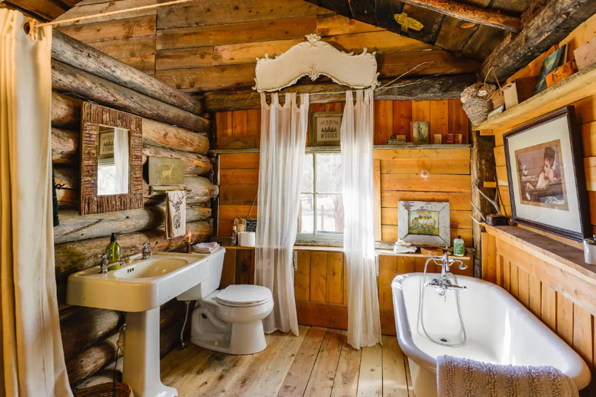 Outside of Lake George, Colorado, a log cabin bathroom features a white, porcelain sink, tub and toilet, along with charming rustic decor.