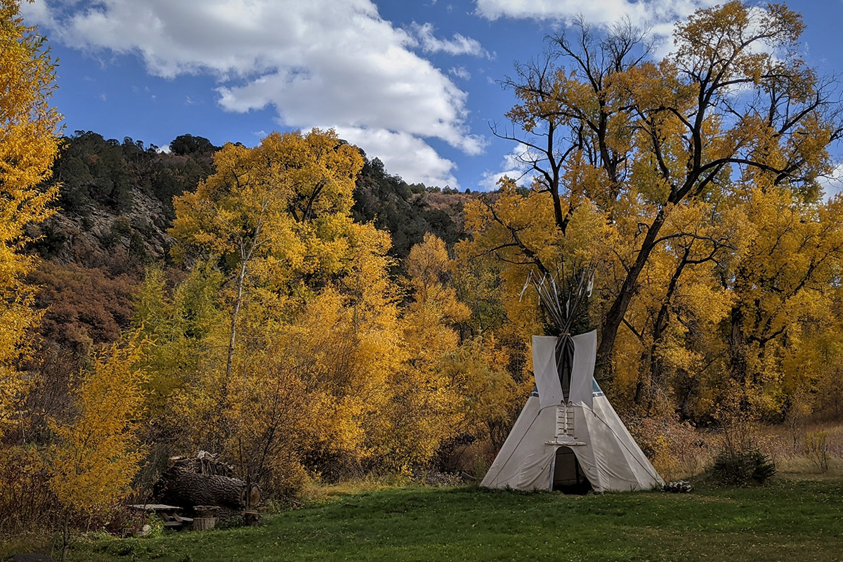 A cone-shape tent sits in a grassy green patch surrounded by amber fall leaves at the Four Mile Creek B&B in Glenwood springs, Colorado.