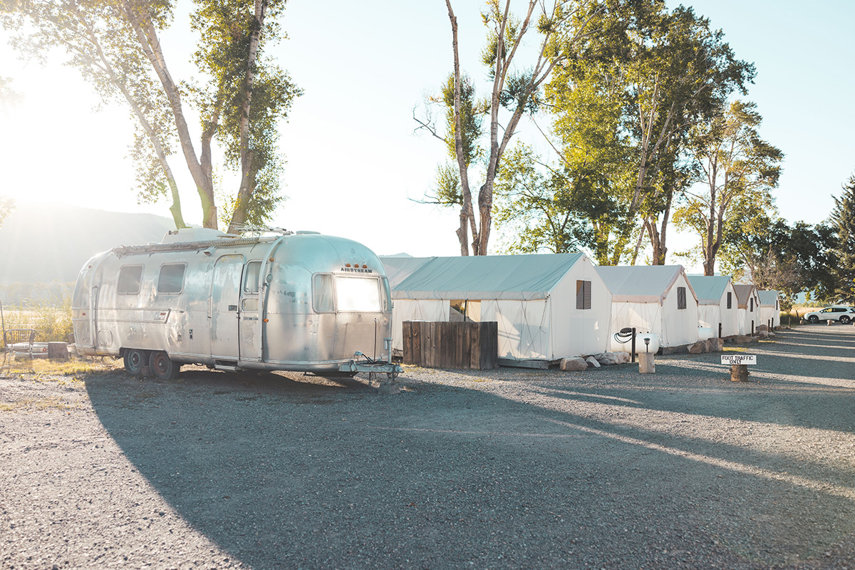 A row of tents at Basecamp 550 in Colorado face towards sun-filled mountain views. At the end of the row sits a shiny metal camper.