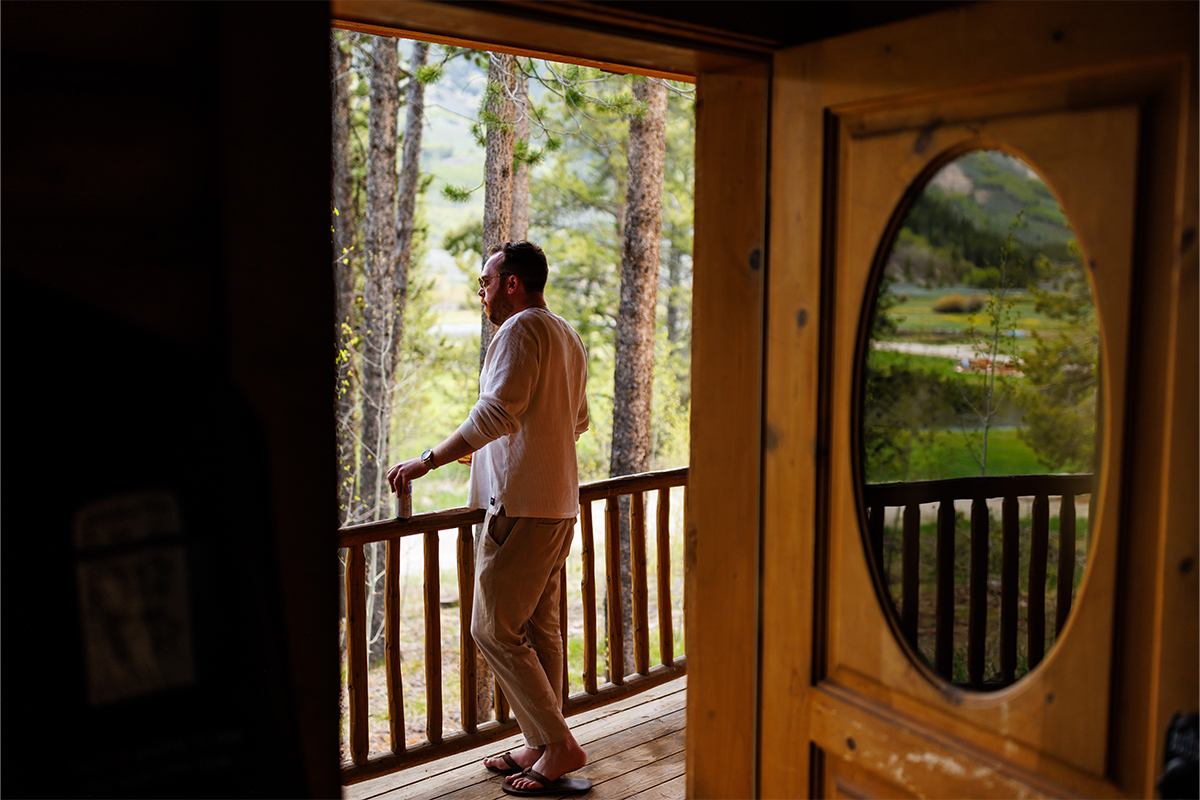 A person admires the view of nature from the wooden porch of a cabin at Camp Hale near Red Cliff, Colorado.