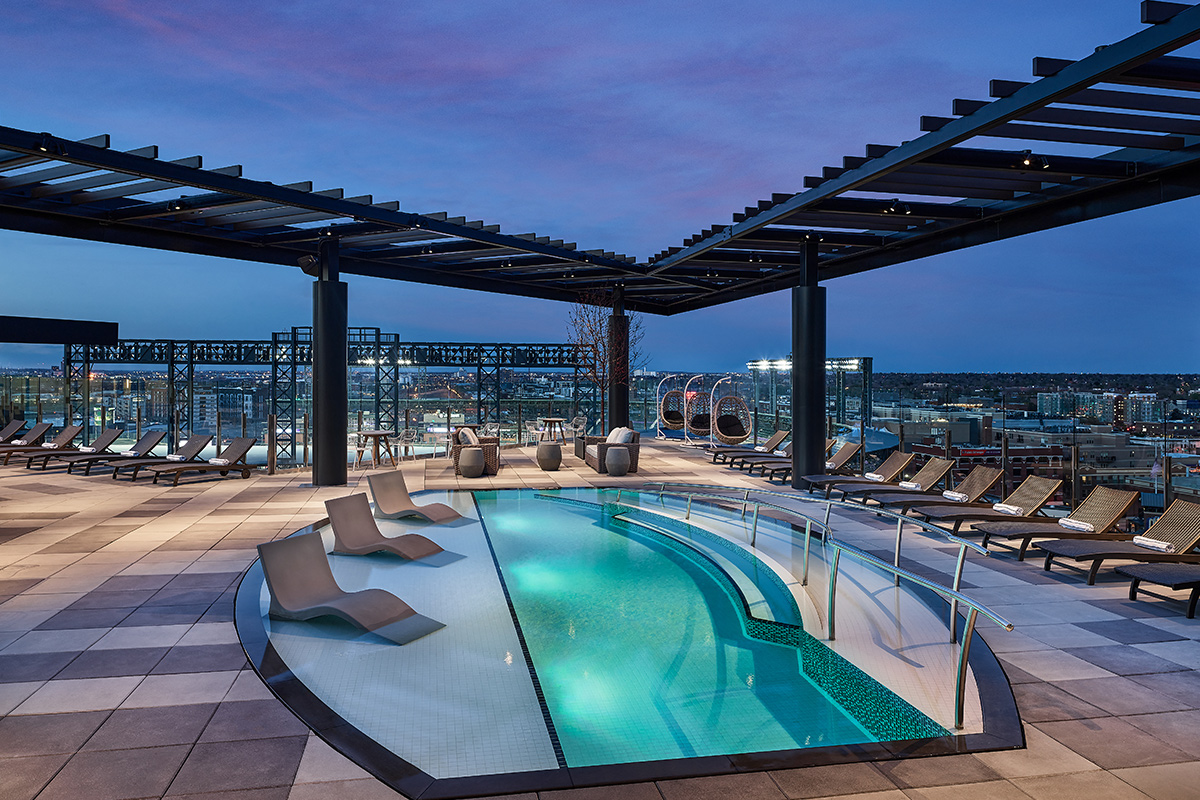 A rooftop pool at The Rally Hotel offers a stunning view of Denver from a number chairs and lounges.