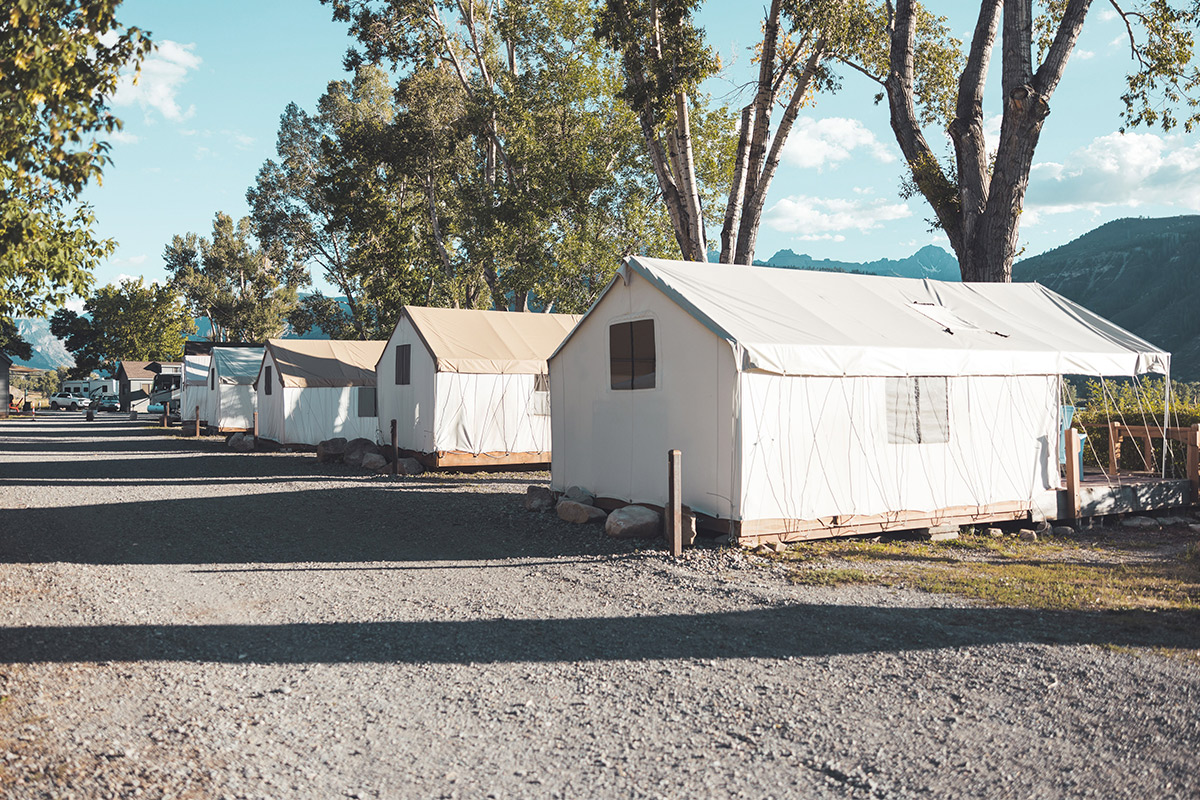 A row of raised glamping tents at Basecamp 550 sit beside a gravel road and face glorious mountain peaks.